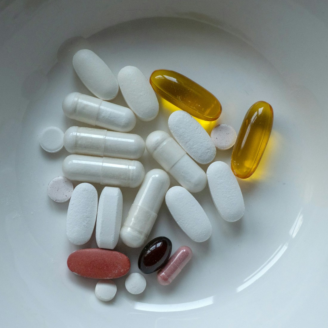 A white bowl containing a variety of supplement capsules and tablets